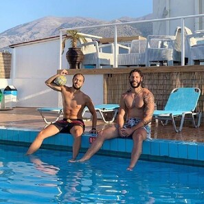 Dos hombres sentados junto a una piscina con montañas al fondo.