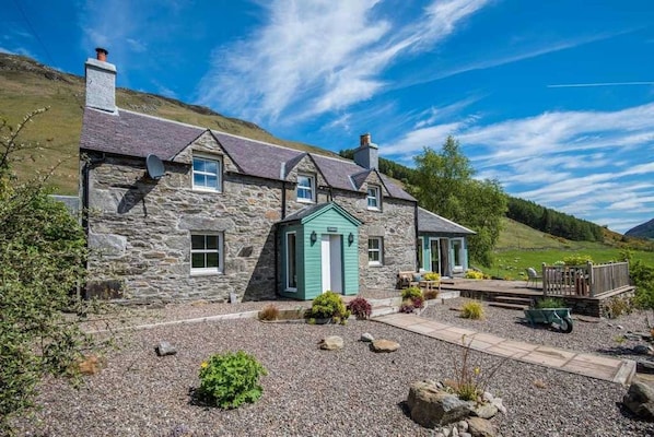 A stone house with a green door, a small porch, and a gravel driveway.