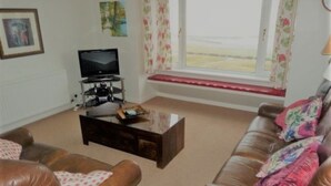 A living room with a brown leather sofa, a television on a stand, and a window with floral curtains.