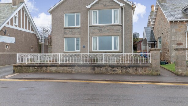 A two-story house with a stone facade, white window frames, and a white fence in front.