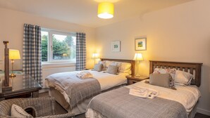 A hotel room with two beds, a window with curtains, a bedside table with a lamp, and a mirror.