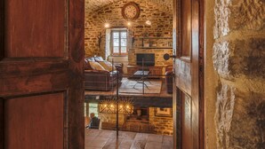 Interior rústico de pedra com porta de madeira, um espaço de estar acolhedor e um relógio visível na parede.