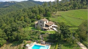 Uma casa de dois andares com piscina, cercada por vegetação exuberante e colinas.