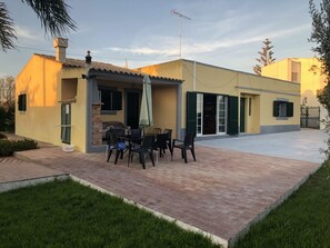 A residential building with a patio area featuring a table and chairs, a covered seating area, and a visible garage door. - Rustic Villa With Pool Near Olhao (Olhao)