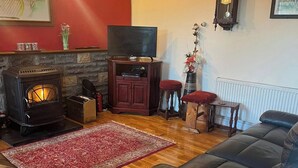 Ein gemütliches Wohnzimmer mit Kamin, Fernseher, Sofa und einer Wanduhr.