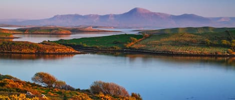 A serene landscape with a lake, rolling hills, and distant mountains.