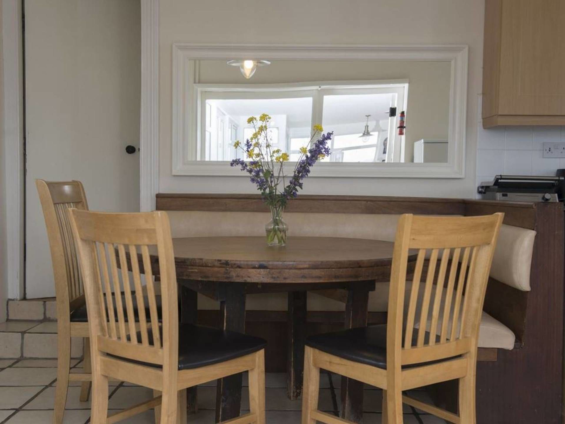A dining area with a round wooden table, two wooden chairs with black cushions, and a vase with flowers.