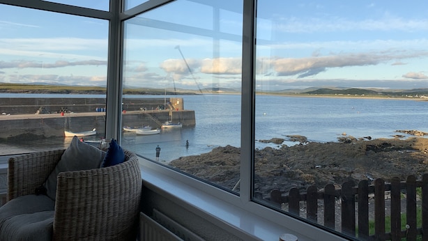 Una habitación con amplios ventanales que dan a un puerto, mobiliario de mimbre y vistas a barcos y una grúa.