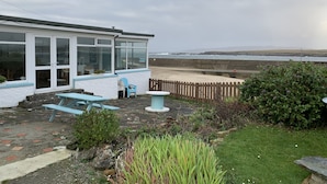 Una casa costera con un invernadero, un patio con mesa y sillas, y vista al mar.
