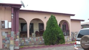 A two-story house with a stone facade, three arched windows, and a large coniferous tree in front. - 3 Bed House Sleeps 6 - Parking, Wifi, Generator (Kumasi)