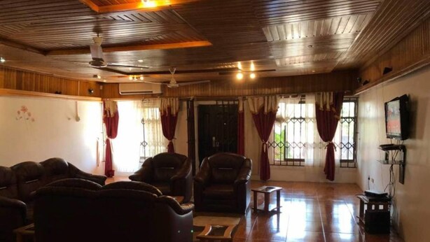 A spacious living room with wooden flooring, leather sofas, a coffee table, and a television mounted on the wall. - 3 Bed House Sleeps 6 - Parking, Wifi, Generator (Kumasi)