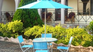 An outdoor seating area with a round table and four blue chairs, surrounded by lush greenery and a blue umbrella. - 3 Bed House Sleeps 6 - Parking, Wifi, Generator (Kumasi)