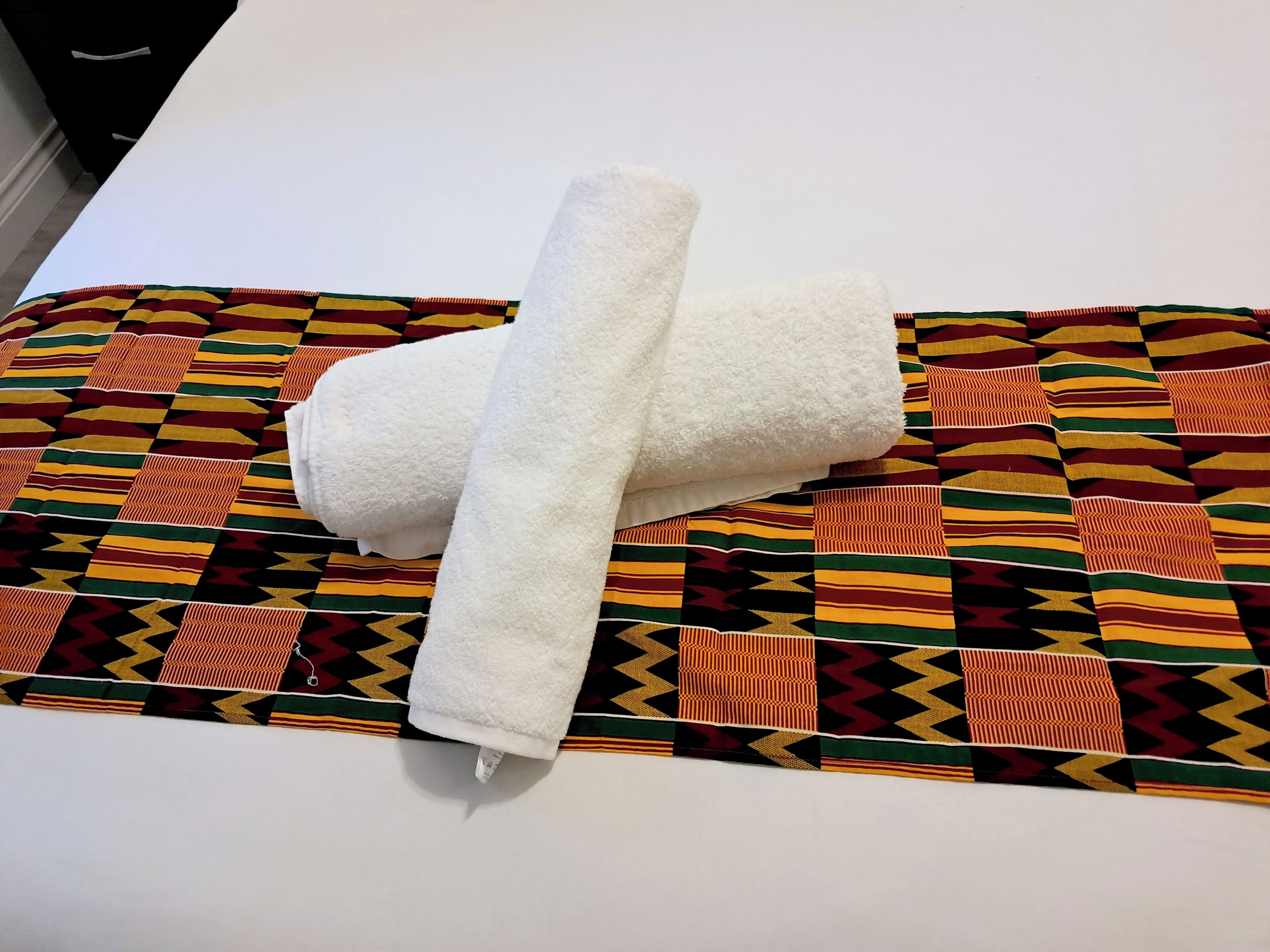 Een witte handdoek ligt gevouwen op een bed met een decoratief laken.