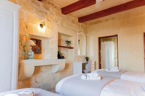 A hotel room with stone walls, a wooden ceiling, a bed, a desk, a mirror, and a bathroom with a shower curtain. - Villa Savona Sleeps 7 With Private Pool (Xaghra)