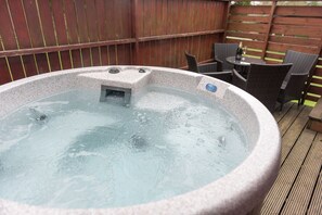 Een hottub met een stenen buitenkant, omringd door rieten stoelen en een kleine tafel met een fles en glas.
