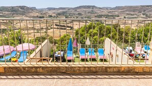 A terrace with a view of a hilly landscape, outdoor seating with umbrellas, and a table with chairs. - Villa Ta Debora Sleeps 7 With Pool (Xaghra)