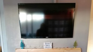 A modern living room with a flat-screen TV mounted above a wooden mantelpiece. Below the mantel, a fireplace with a black stove and logs is visible. - Sea View Retreat - Free Wifi (Bridlington)