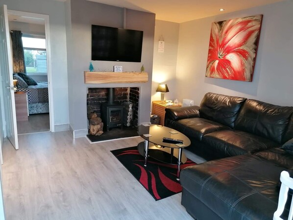 A living room with a fireplace, a leather sofa, a coffee table, and a flat-screen TV mounted on the wall.