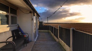 A covered outdoor area with a bench, a wooden deck, and a view of a field under a cloudy sky. - Sea View Retreat - Free Wifi (Bridlington)