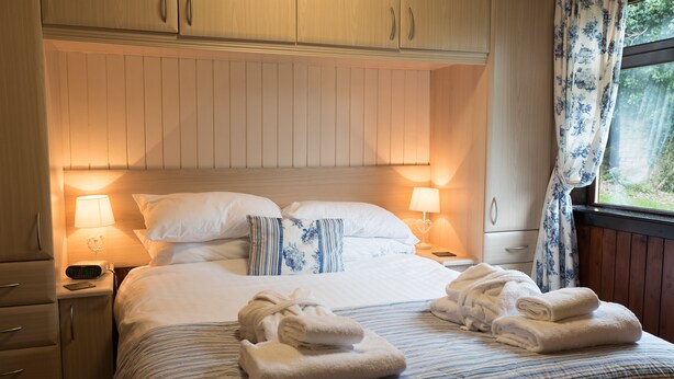 A hotel room with a bed, two bedside tables, a nightstand, a lamp, and a window with curtains. - Birch Lodge 23 With Hot Tub, Newton Stewart (Newton Stewart)