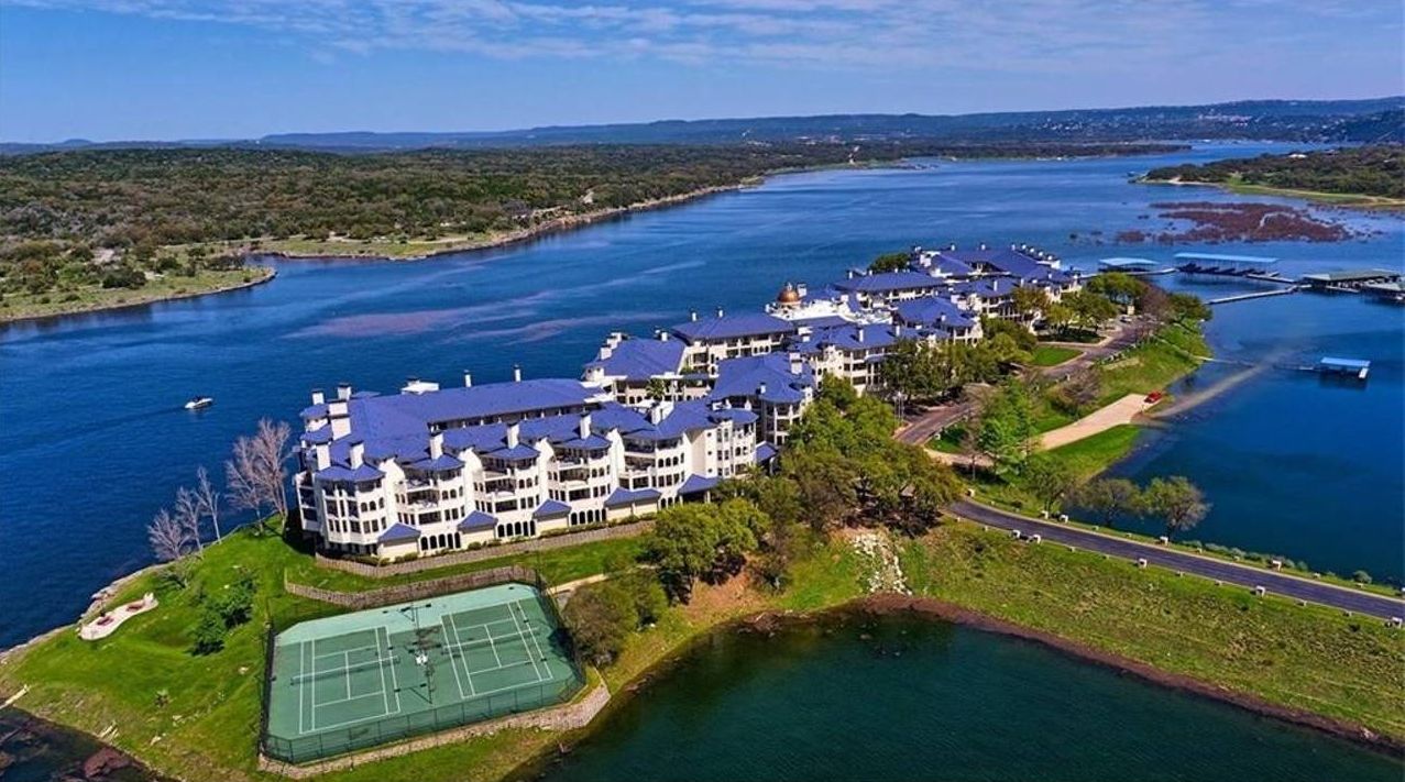 Een luchtbeeld van een groot hotel met meerdere verdiepingen, een tennisbaan en een ligging nabij water.