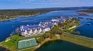 Oversigtsbillede af et stort, mangeetagers hotel med tennisbane, beliggende nær vandet.