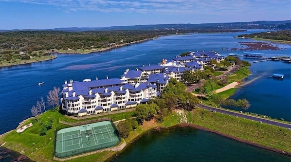 An aerial view of a large, multi-story hotel with a tennis court, located near a body of water.