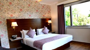 Une chambre d’hôtel avec un grand lit, deux lampes de chevet, une table de chevet avec un téléphone et une fenêtre avec des rideaux.