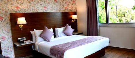 Habitación de hotel con una cama grande, dos lámparas de noche, una mesita de noche con teléfono y una ventana con cortinas.