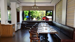 Un restaurant doté d’une longue table en bois, de banquettes en cuir et offrant une vue sur la verdure environnante.
