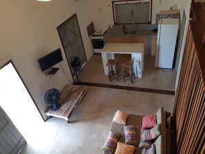 A compact living space with a kitchenette, a dining area with stools, a sofa with cushions, and a TV mounted on the wall.