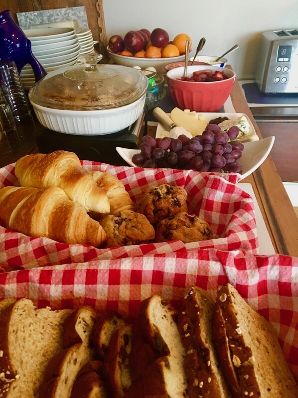 A breakfast buffet with croissants, muffins, bread, grapes, and cheese.