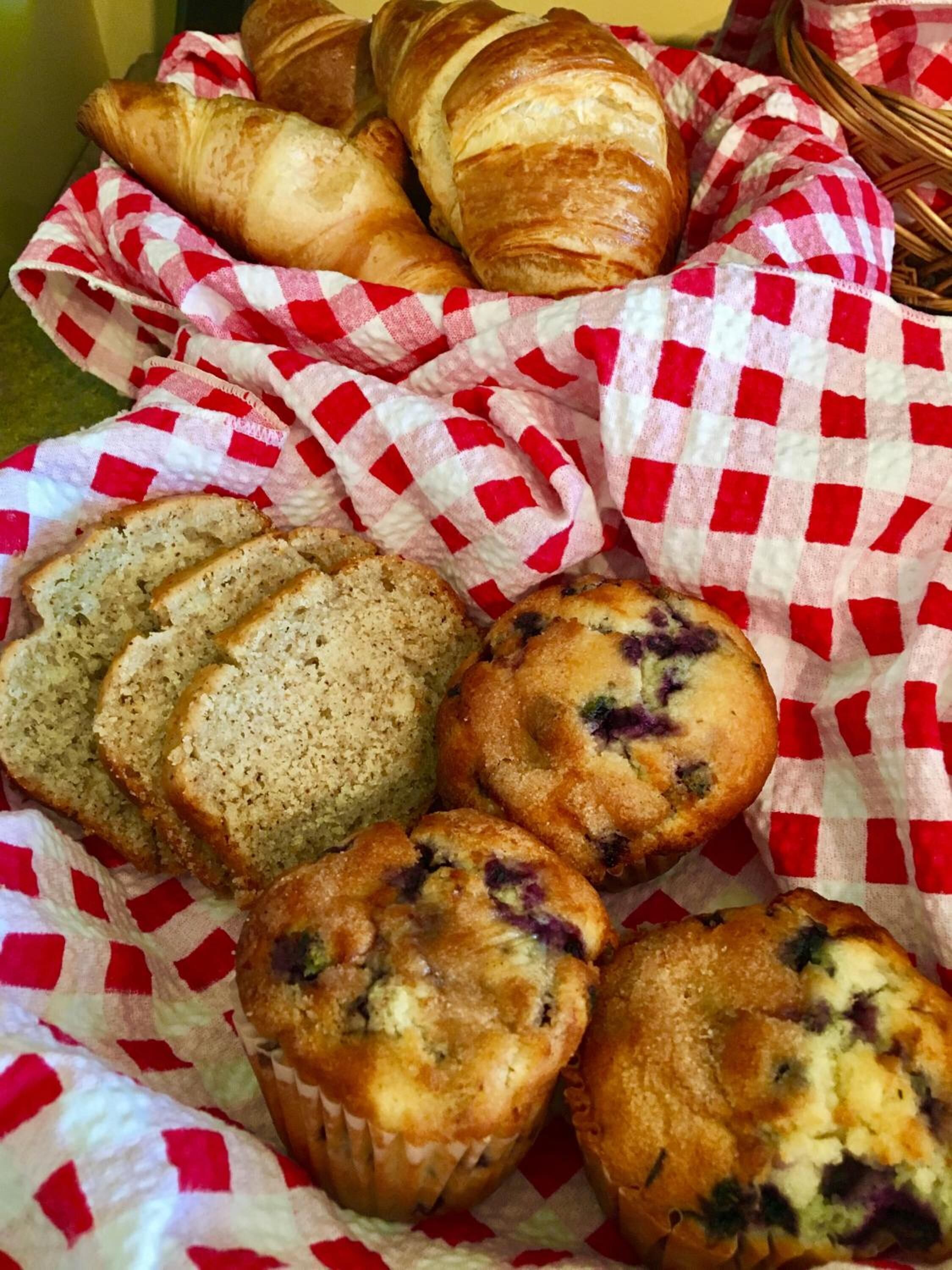 Un panier rempli de viennoiseries, notamment des croissants, des muffins et du pain tranché.