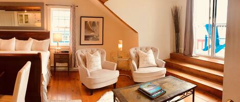 Una habitación acogedora con una cama, dos sillones, una mesa de centro y un ventanal con vistas al exterior.