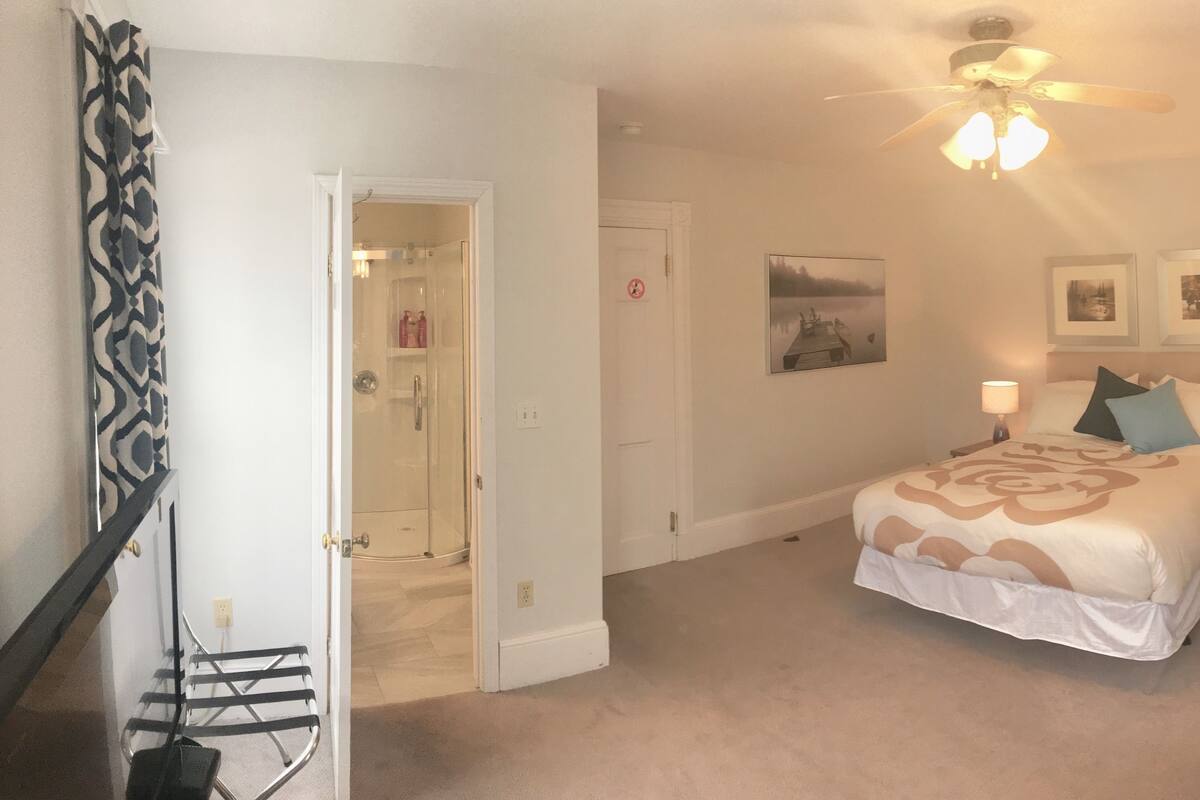 A bedroom with a bed, two bedside tables, a chair, a ceiling fan, and a window.