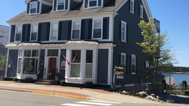 A two-story building with a dark facade and white trim, featuring a prominent entrance with a sign for 'Treadwell Inn' and a flag.