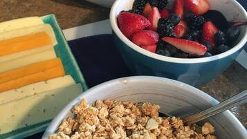 A breakfast table with bowls of granola, fresh fruits, and sliced cheese.