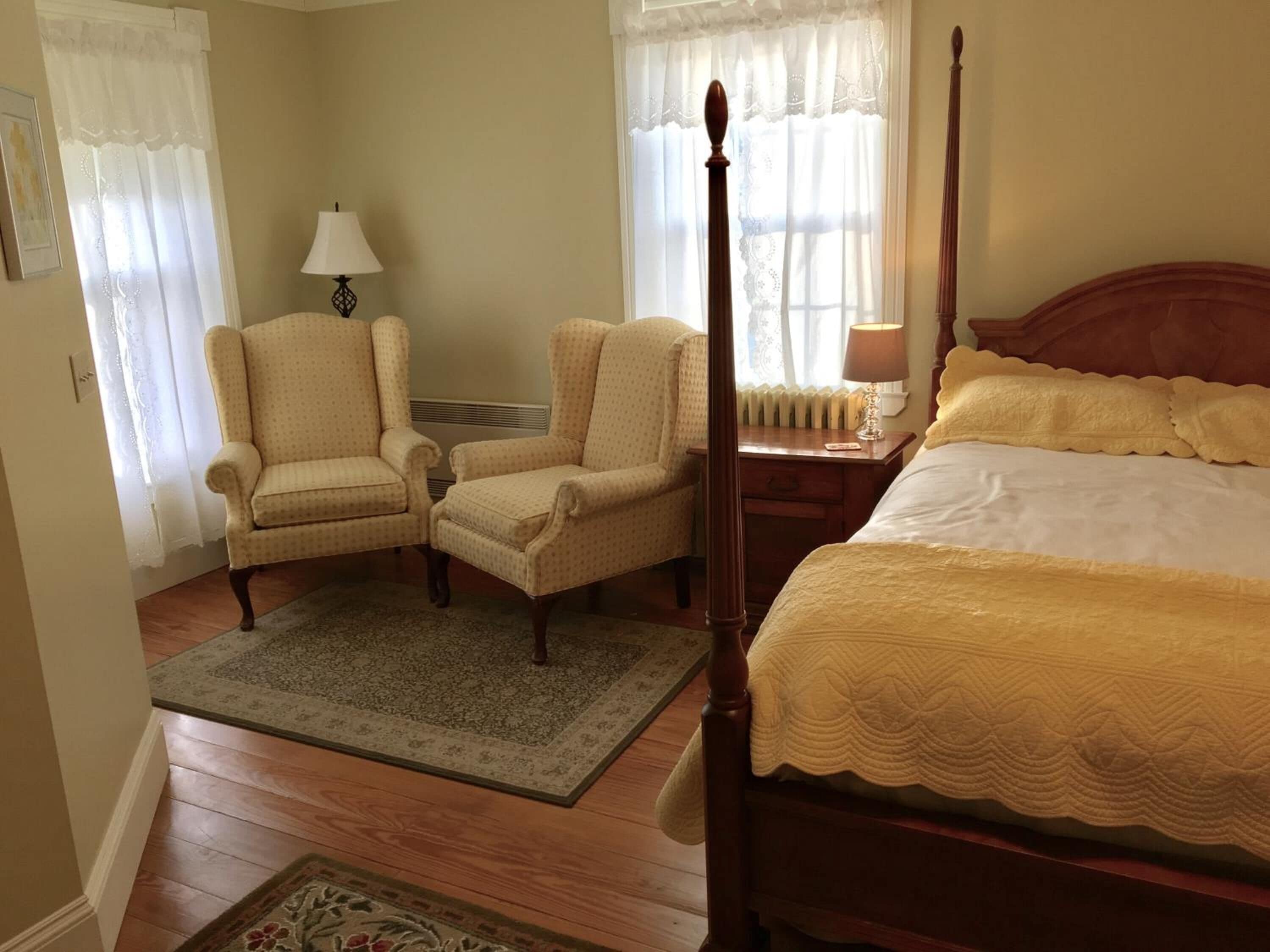 A bedroom with a four-poster bed, two armchairs, a nightstand, and a lamp.