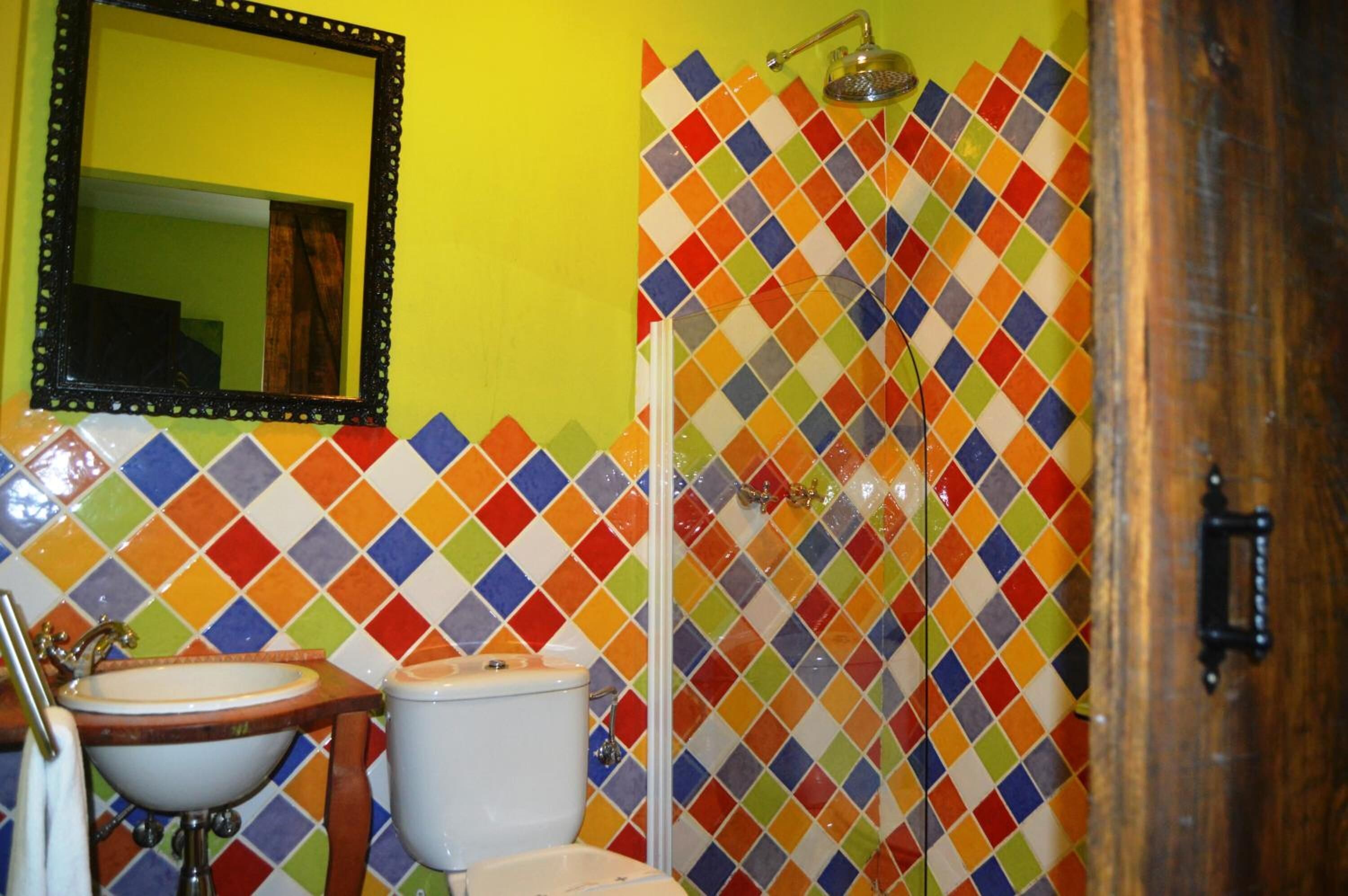 A bathroom with a colorful mosaic tile wall, a sink, and a toilet.