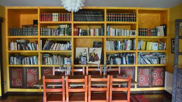A room with a large bookshelf filled with books, a wooden dining table with chairs, and patterned wall panels.