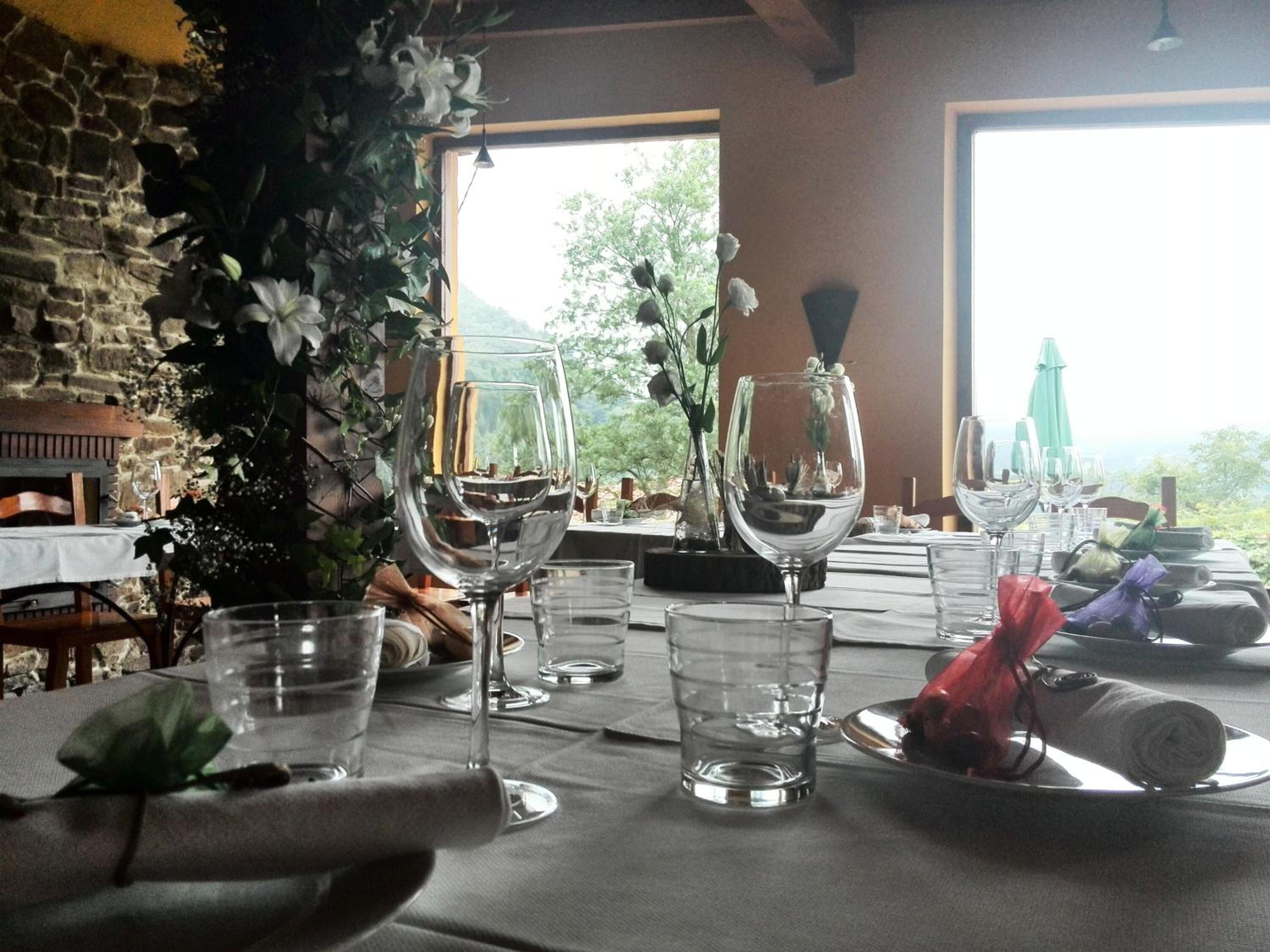Une table à manger dressée avec des verres à vin, des verres à eau et des assiettes, donnant sur un paysage verdoyant.