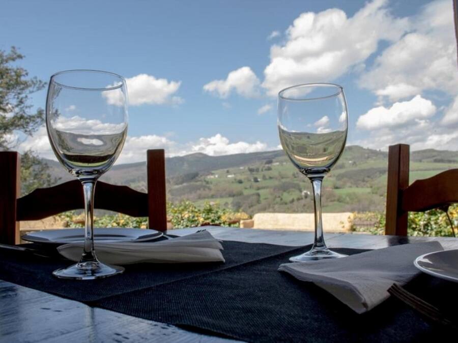 Dos copas de vino vacías sobre una mesa, con vistas a colinas verdes y un cielo despejado.