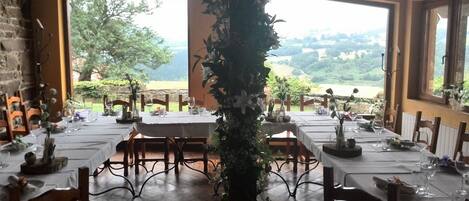 A dining area with tables set for a meal, large windows offering a view of the countryside, and a central decorative pillar.