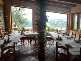 Un comedor con mesas dispuestas para una comida, ventanas amplias que ofrecen vistas al campo y un pilar decorativo central.