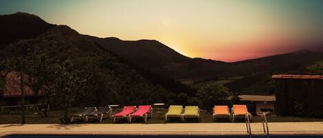 A poolside area with lounge chairs and a view of mountains during sunset.