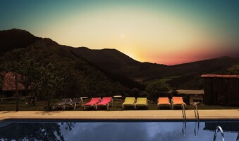 Zona de piscina con sillones de descanso y vistas a las montañas al atardecer.