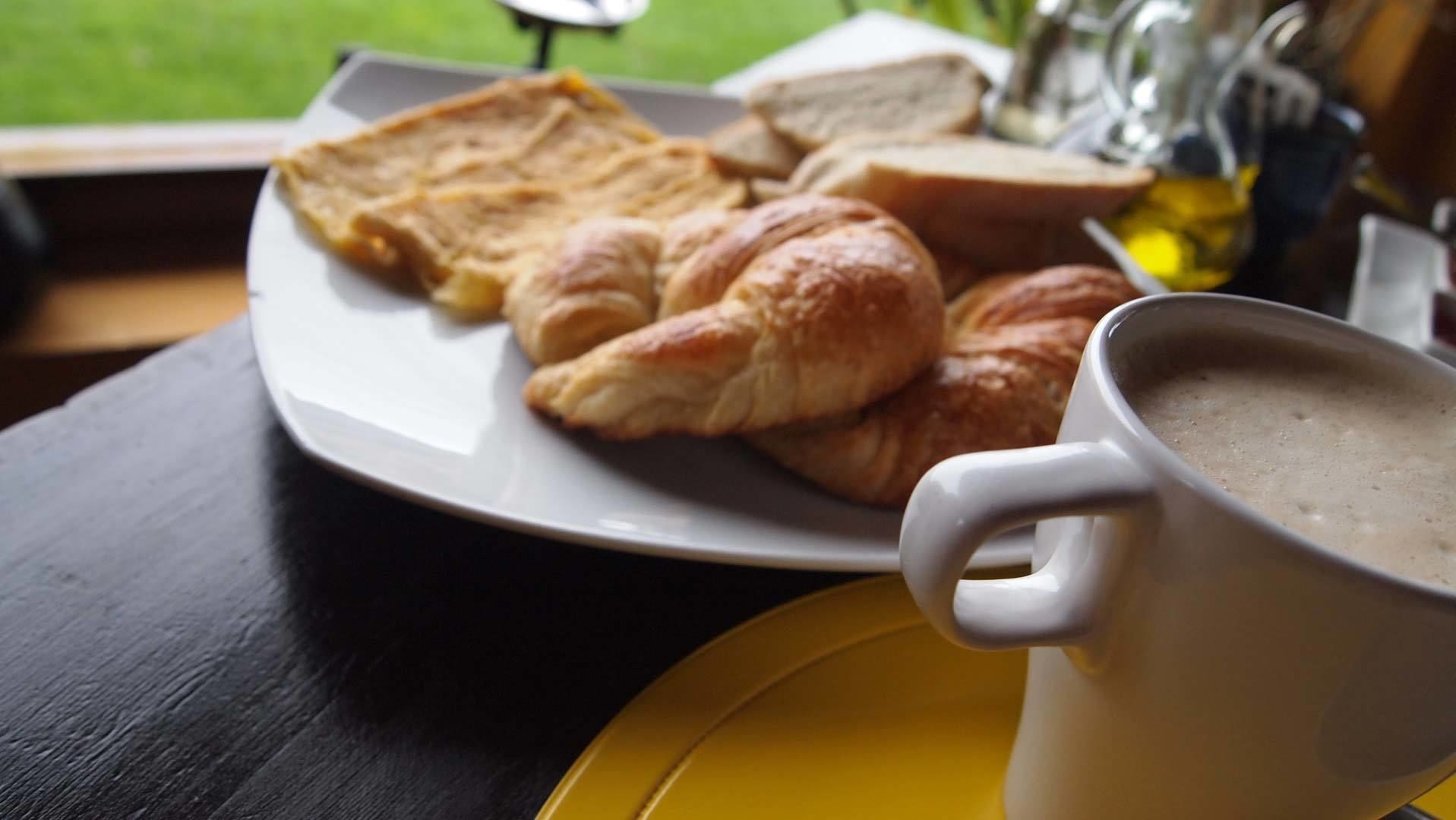 Une assiette avec des croissants et du pain, une tasse de café et une soucoupe jaune sur une table.