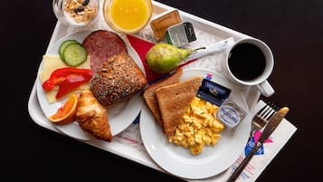 A breakfast tray with toast, scrambled eggs, a croissant, a slice of cheese, a red bell pepper, a cucumber, a sausage, a pear, a glass of orange juice, a cup of coffee, and a small container of jam.