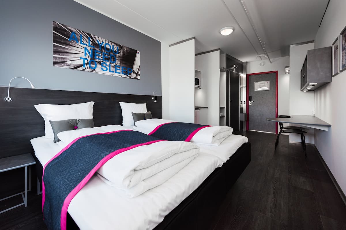 A modern hotel room with two beds, a desk, and a bathroom.