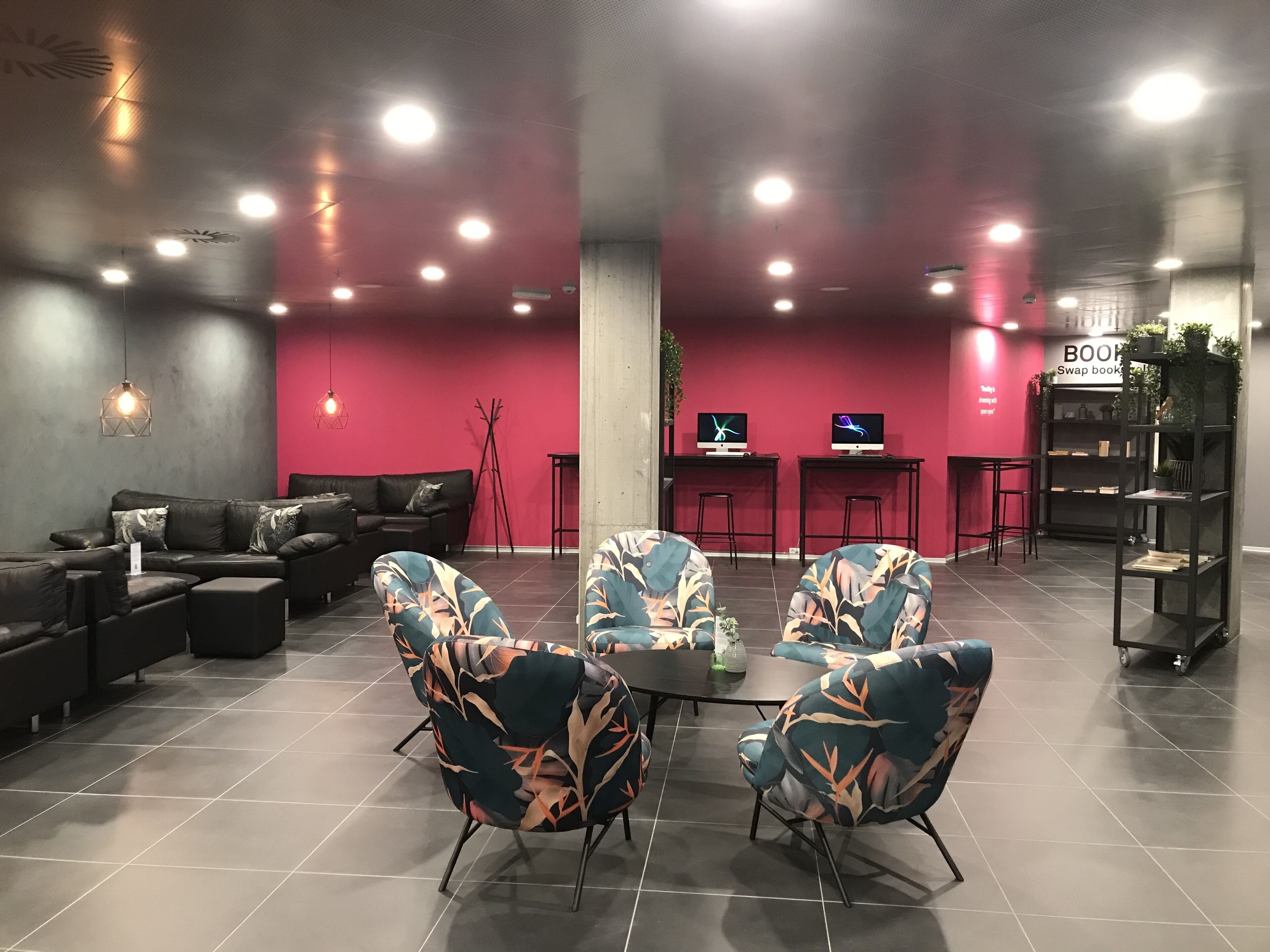 A modern lounge area with a black leather sofa, patterned armchairs, a coffee table, and a bookshelf.